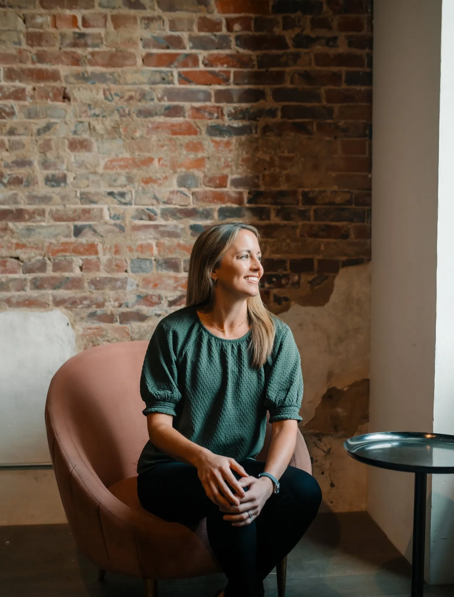 Megan Roberts, smiling, seated beside a brick wall.